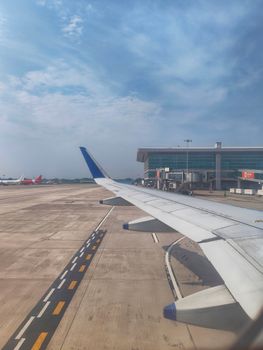 View from airplane window showing airport runway and terminal on a sunny day.
