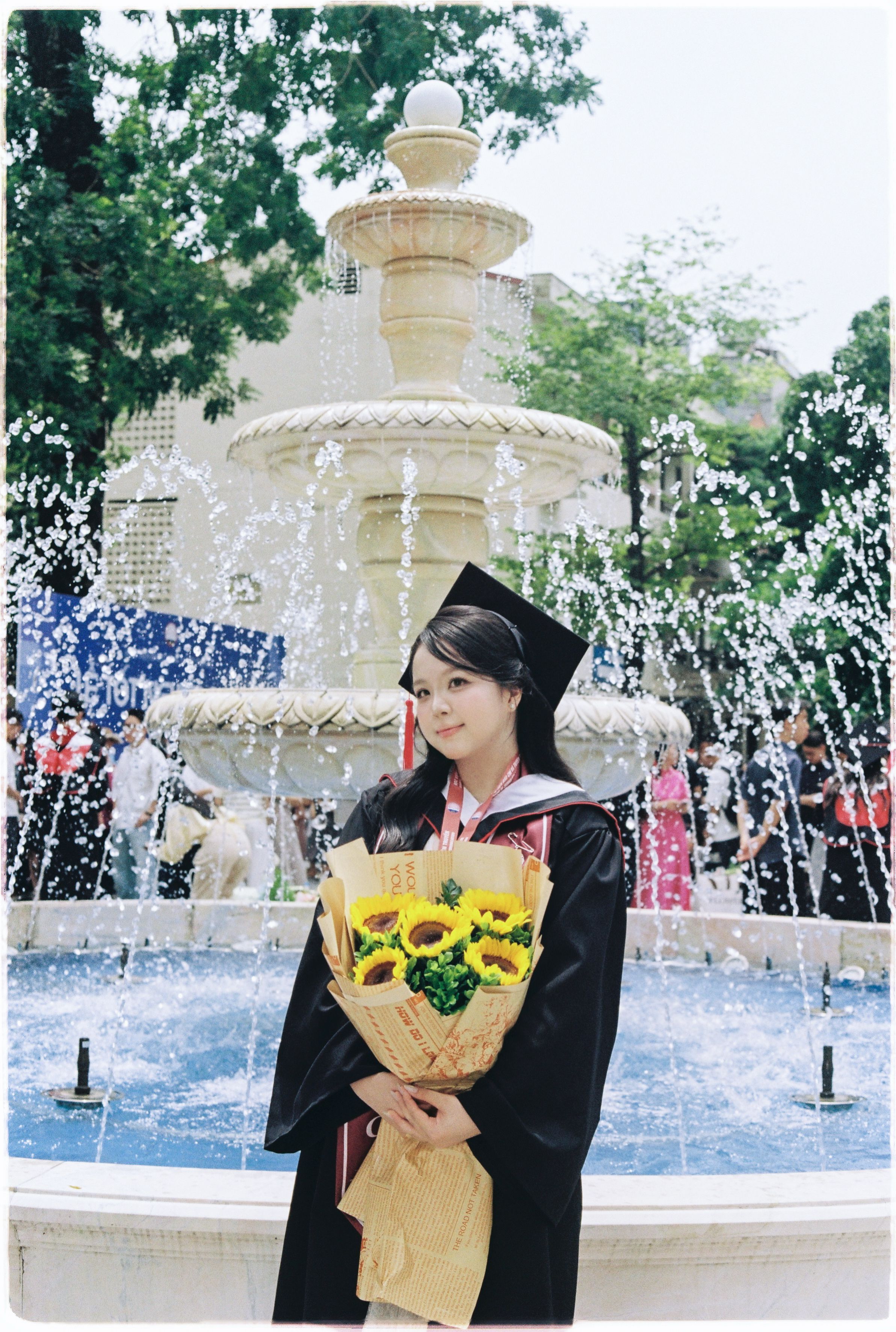 Young graduate with bouquet at a fountain, capturing a celebratory moment outdoors.