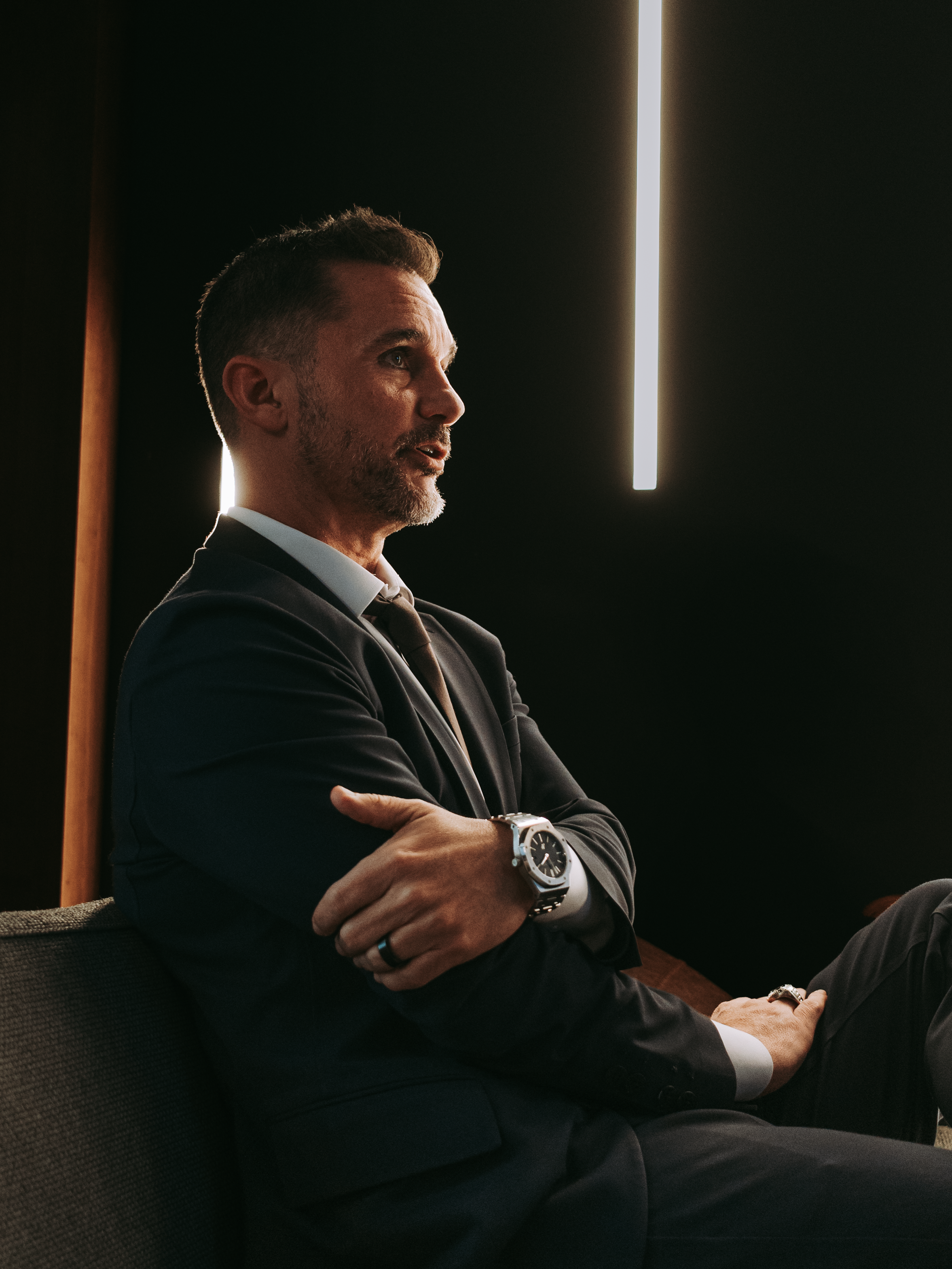 Side profile of a confident man in a suit with a luxury watch, illuminated by bold lighting.