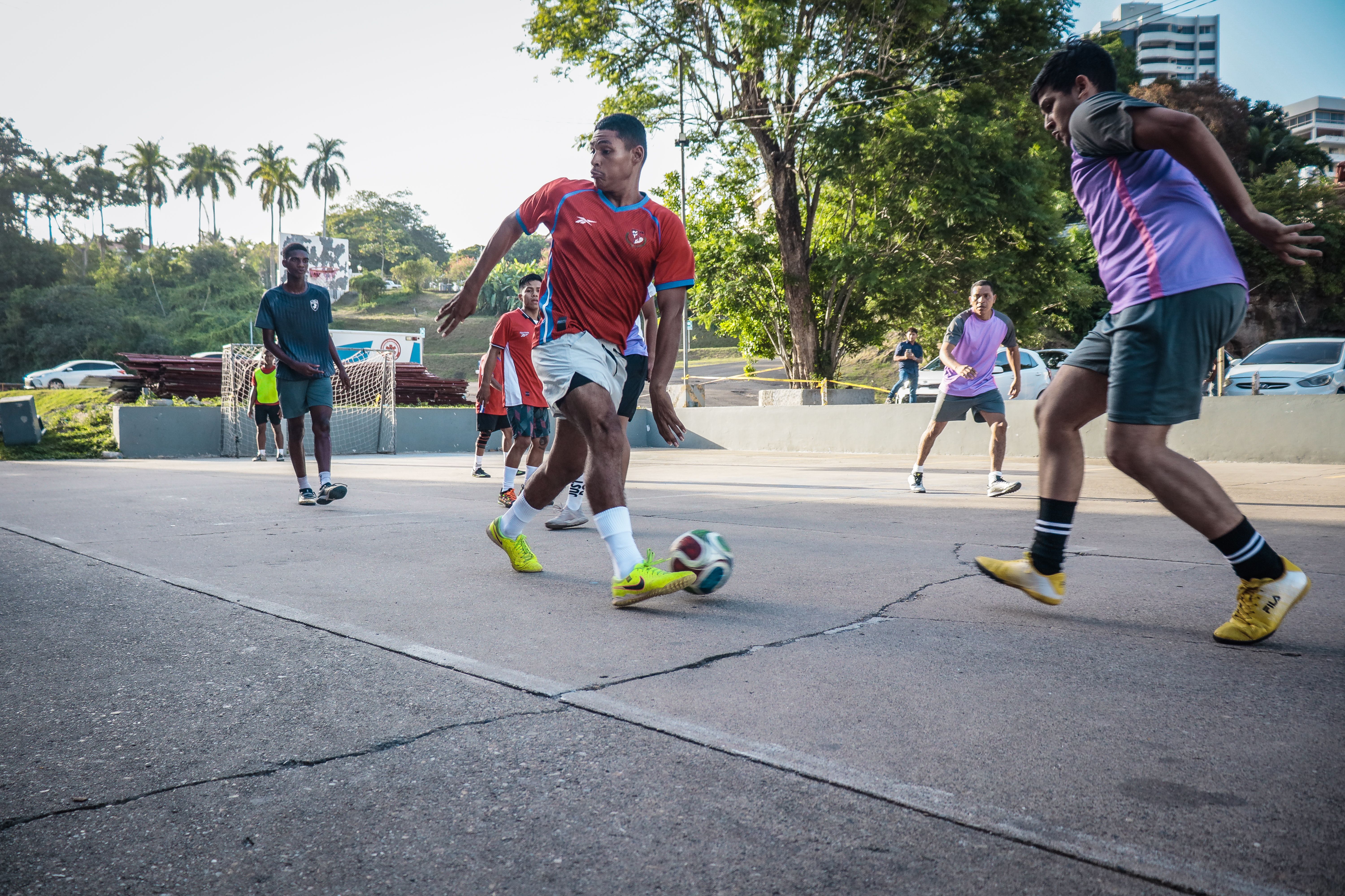 Amateur players compete in an intense street football match on a sunny day.