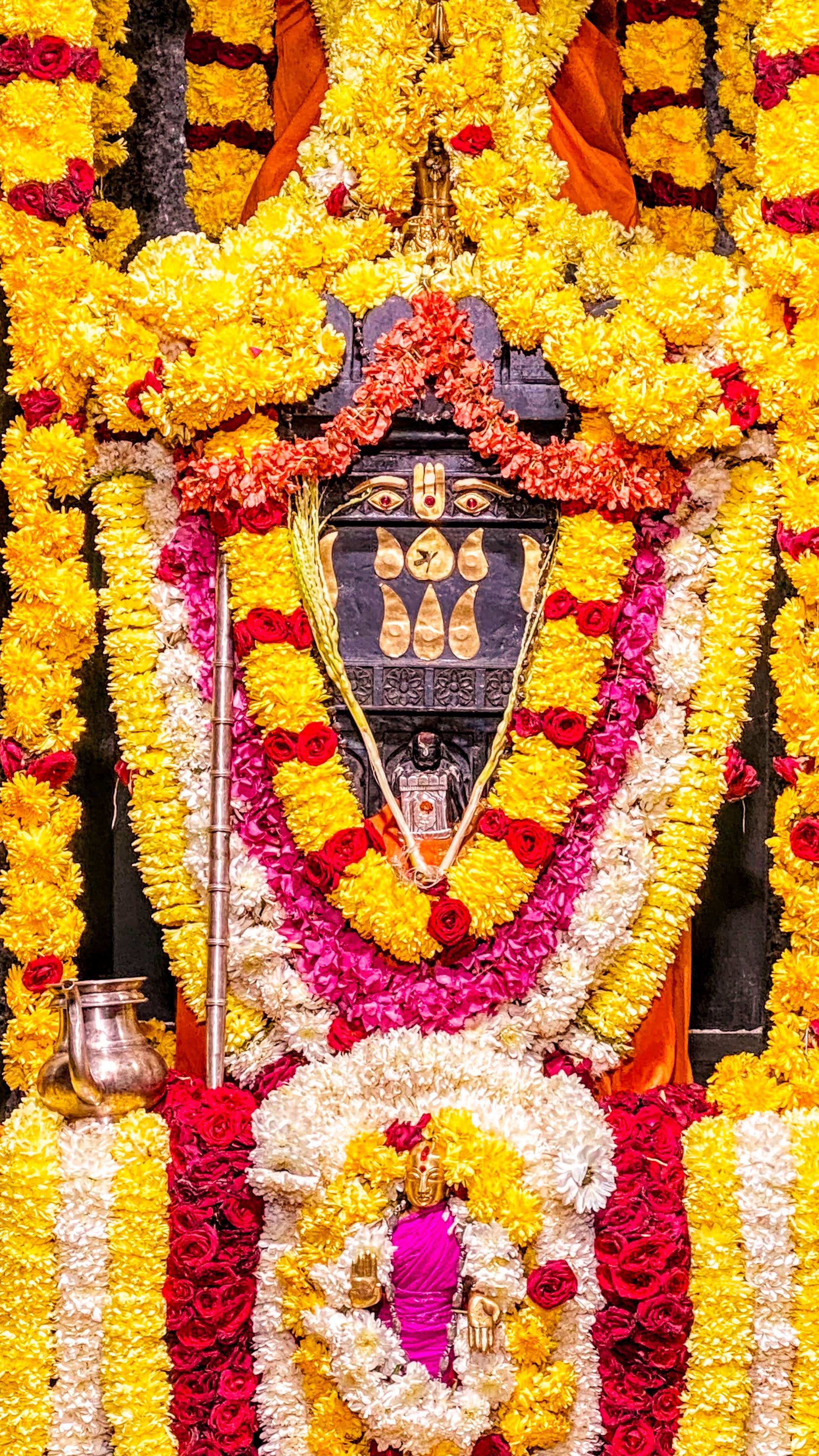 Vibrant arrangement of yellow and red flowers adorning a temple deity in Karnataka, India.
