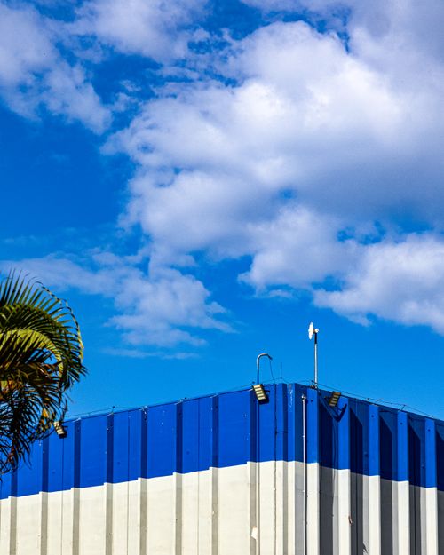 Free Modern industrial building with blue accents against a vibrant blue sky, showcasing clear architectural lines. Stock Photo