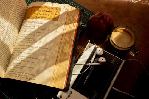 Free A cozy scene with a vintage book, earphones, coffee, and peach on a wooden desk. Stock Photo