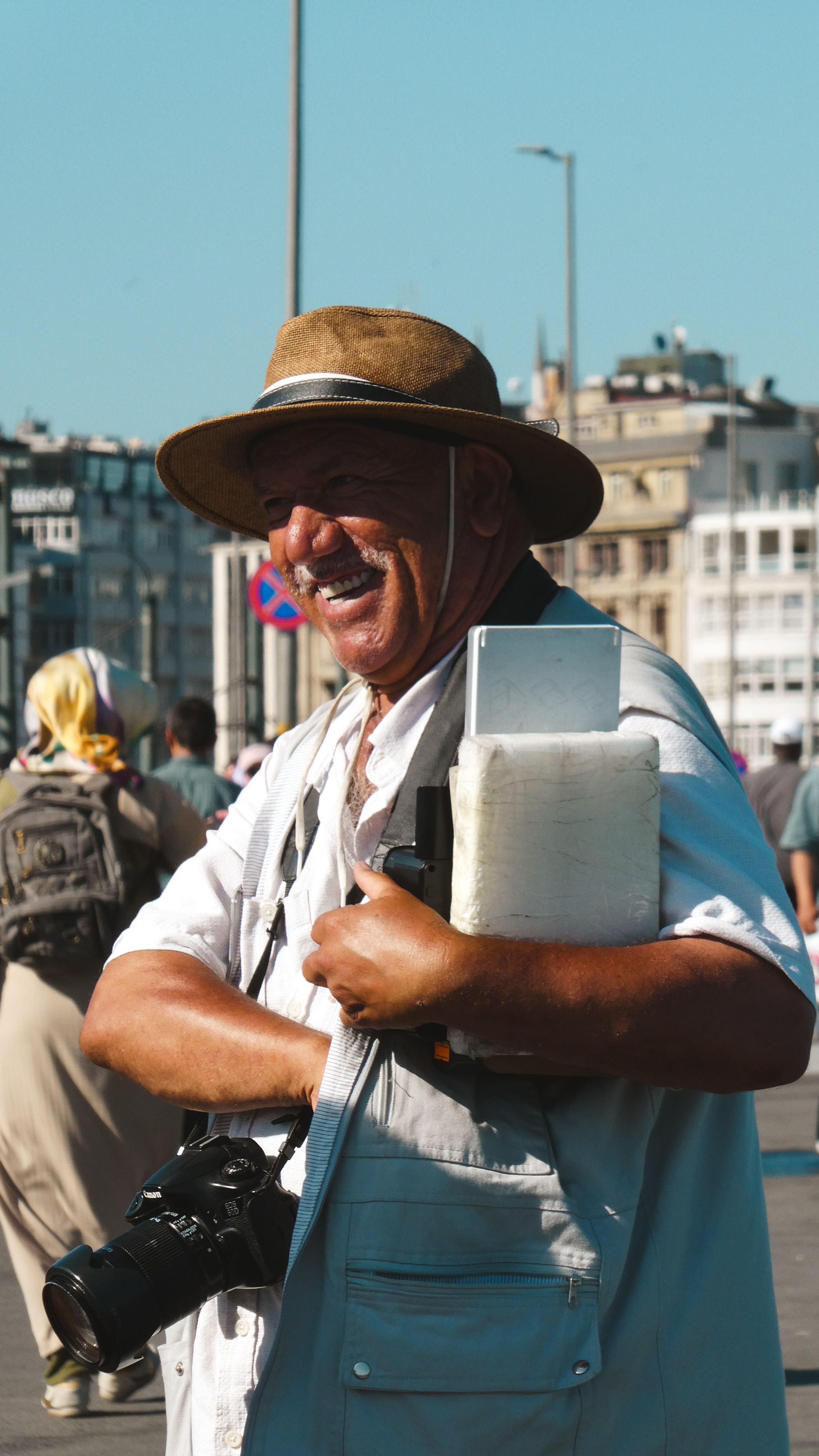 Cheerful man with a camera and equipment in a bustling city street during daytime.