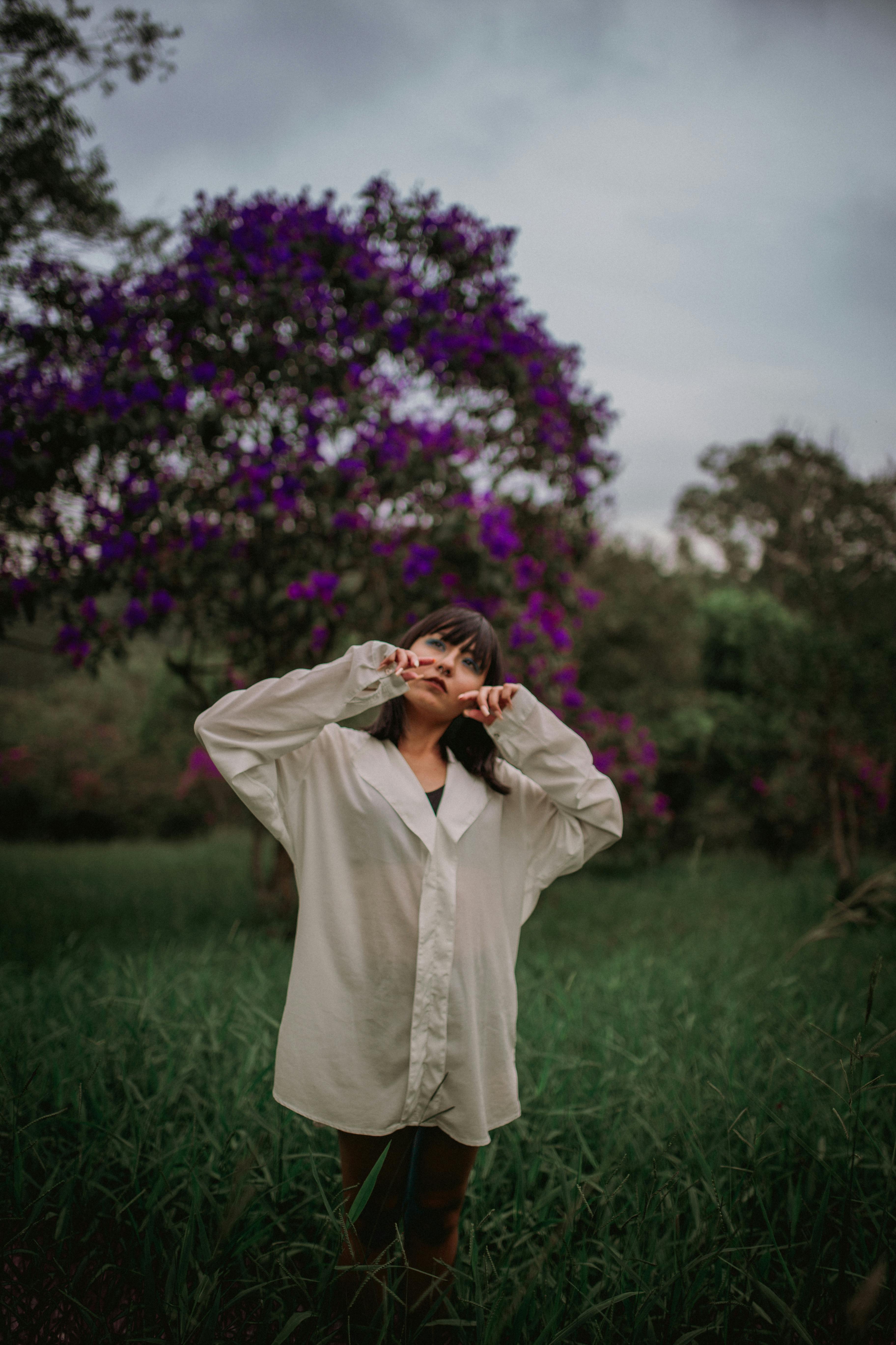 一位年轻女子在绿意盎然的田野中时尚摆拍，身后是开花的树木