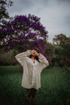 一位年轻女子在绿意盎然的田野中时尚摆拍，身后是开花的树木