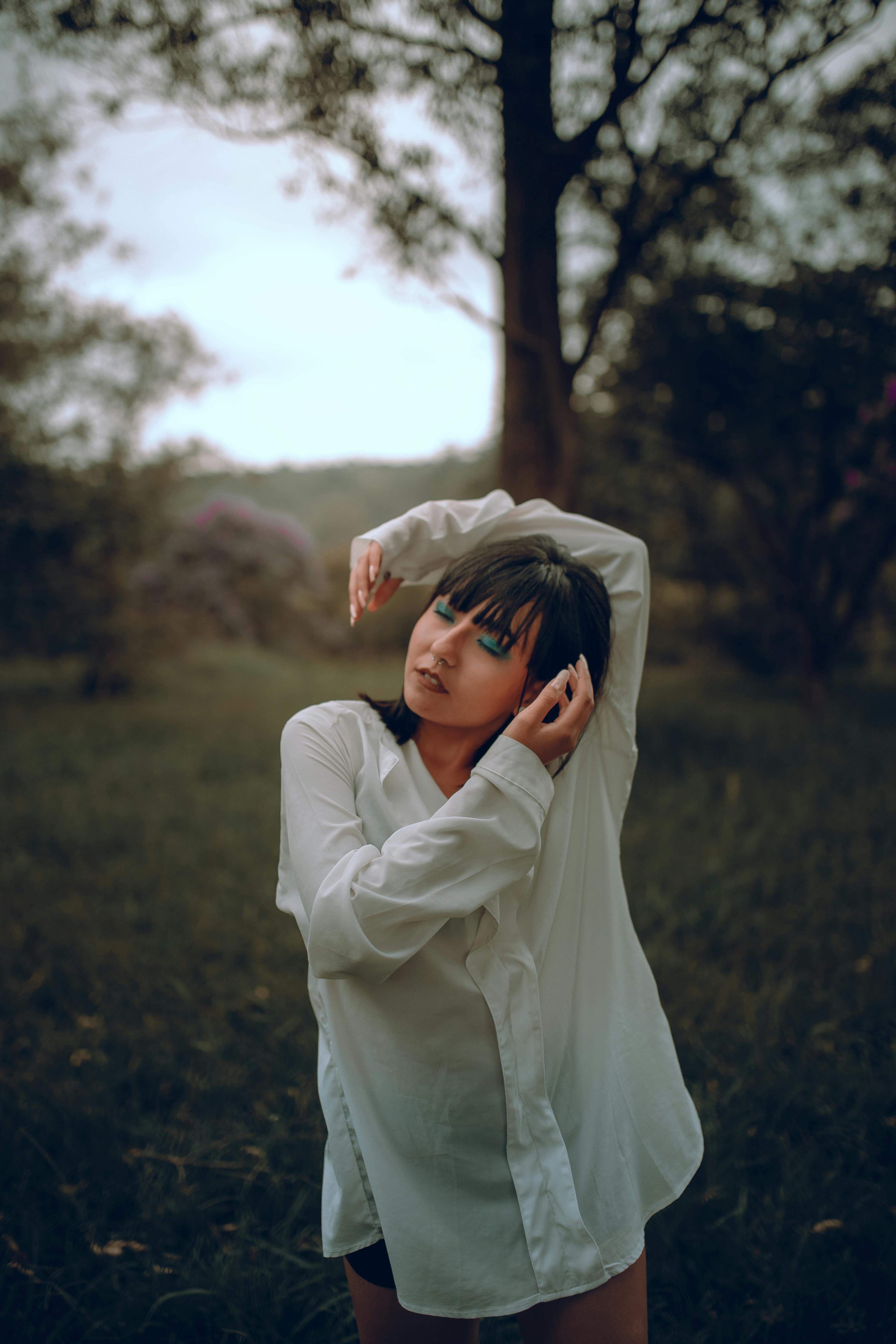 一位年轻女子穿着白衬衫，背景是模糊的森林