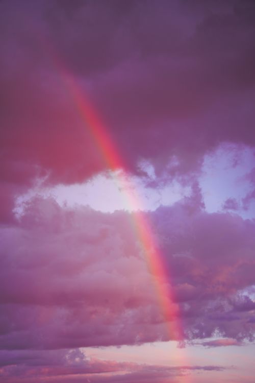Free A stunning rainbow arches through dramatic purple and pink clouds during a vibrant sunset. Stock Photo