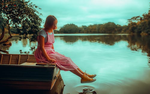 Ragazza In Vestito Rosa Che Si Siede Sul Bacino Di Legno Marrone