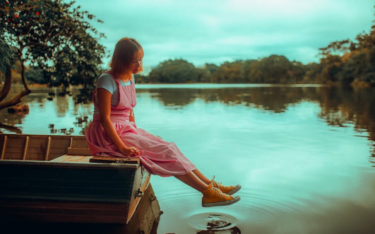 Young Woman In Pink Dress Sitting On Brown Boat