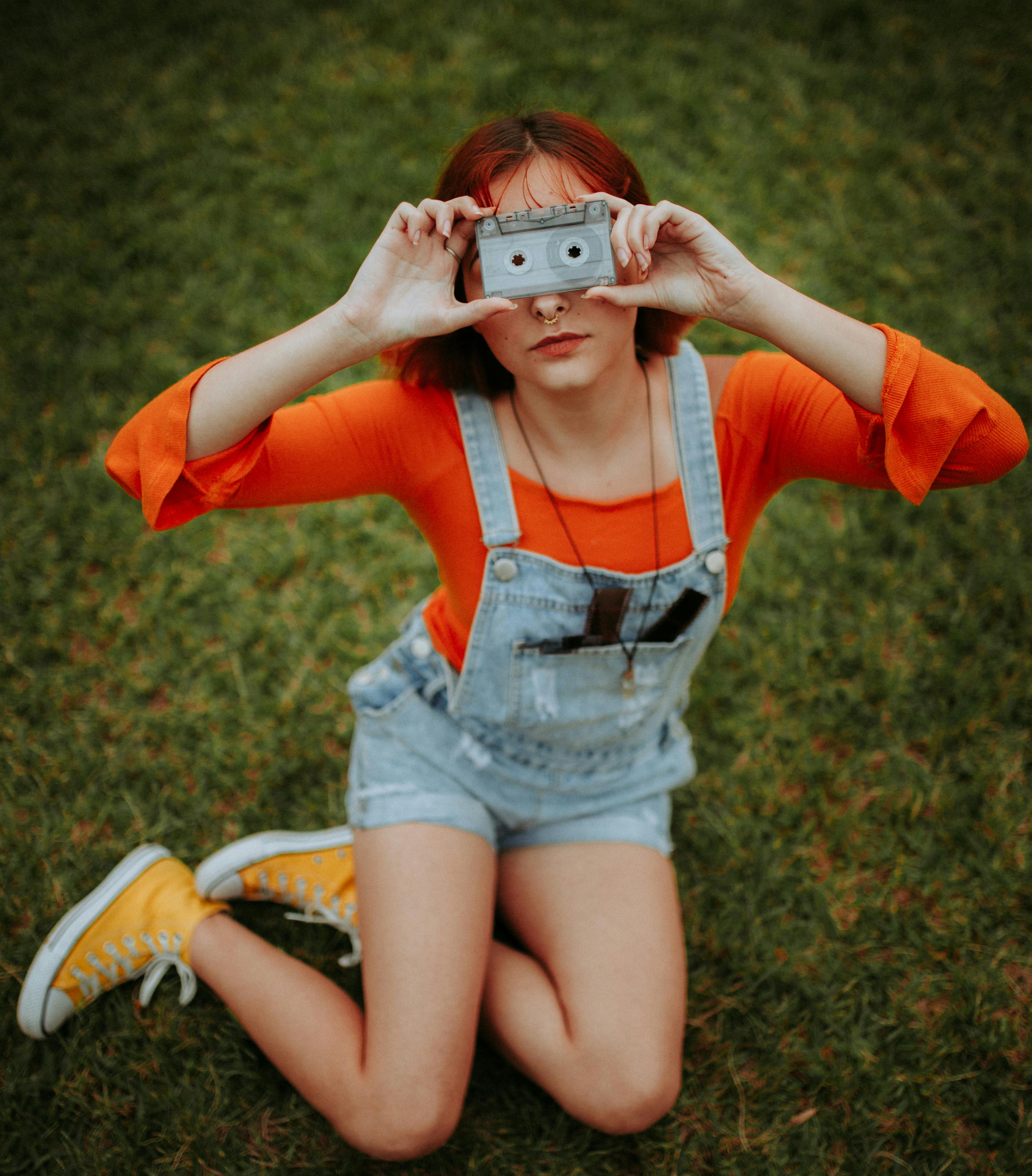 young woman sitting on the grass while holding a cassette tape