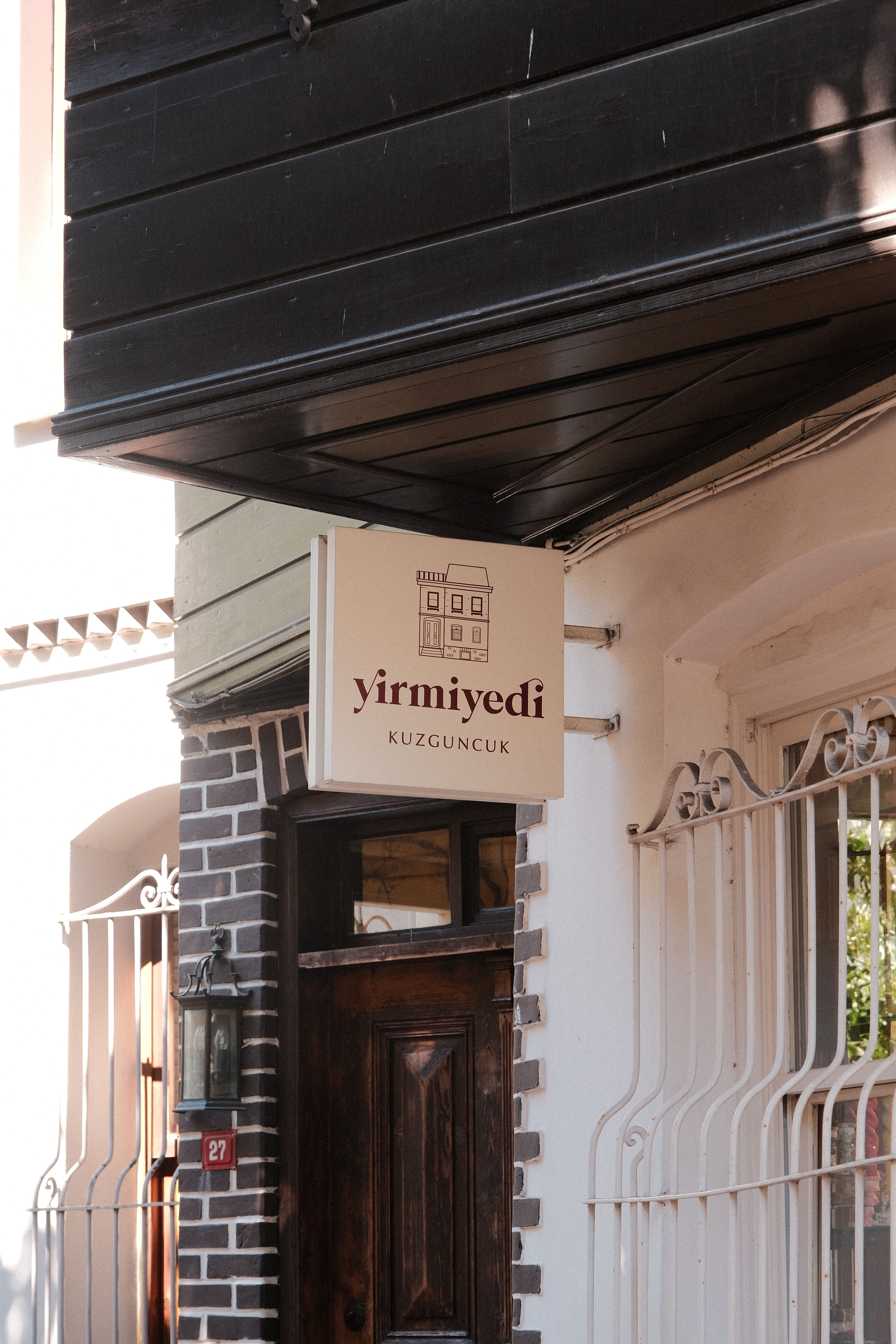 A stylish café entrance with a sign reading 'Yirmiyedi Kuzguncuk' in natural daylight.