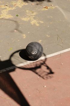 A basketball rests on an outdoor court with shadow of a hoop.