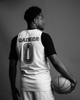 Monochrome image of a male basketball player holding a ball, showing his jersey from behind.