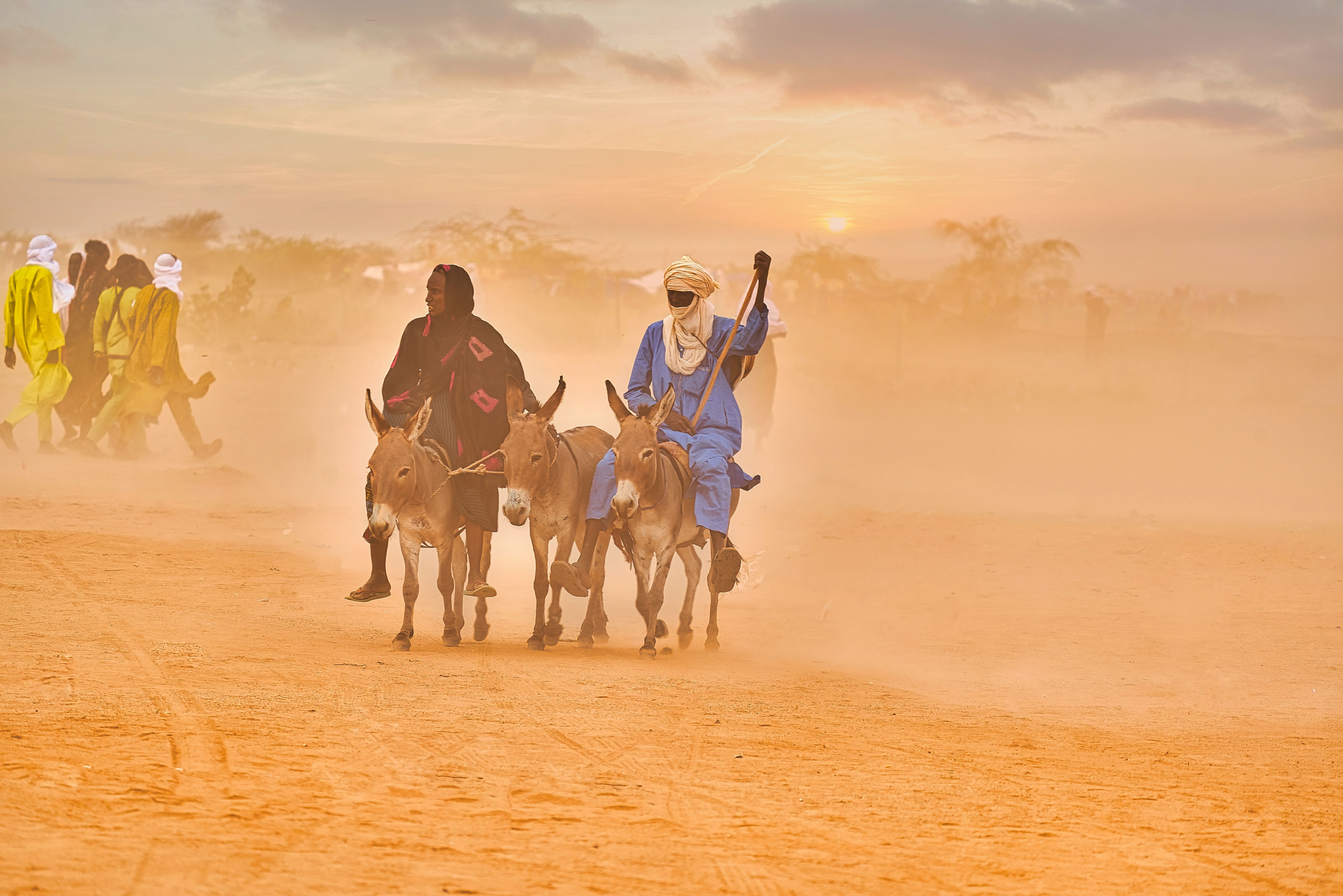 Two men riding donkeys through the dust in Agadez, showcasing traditional attire and desert culture.