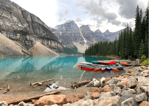 Canoes on Brown Rocky Shore Near Green Trees and Mountains