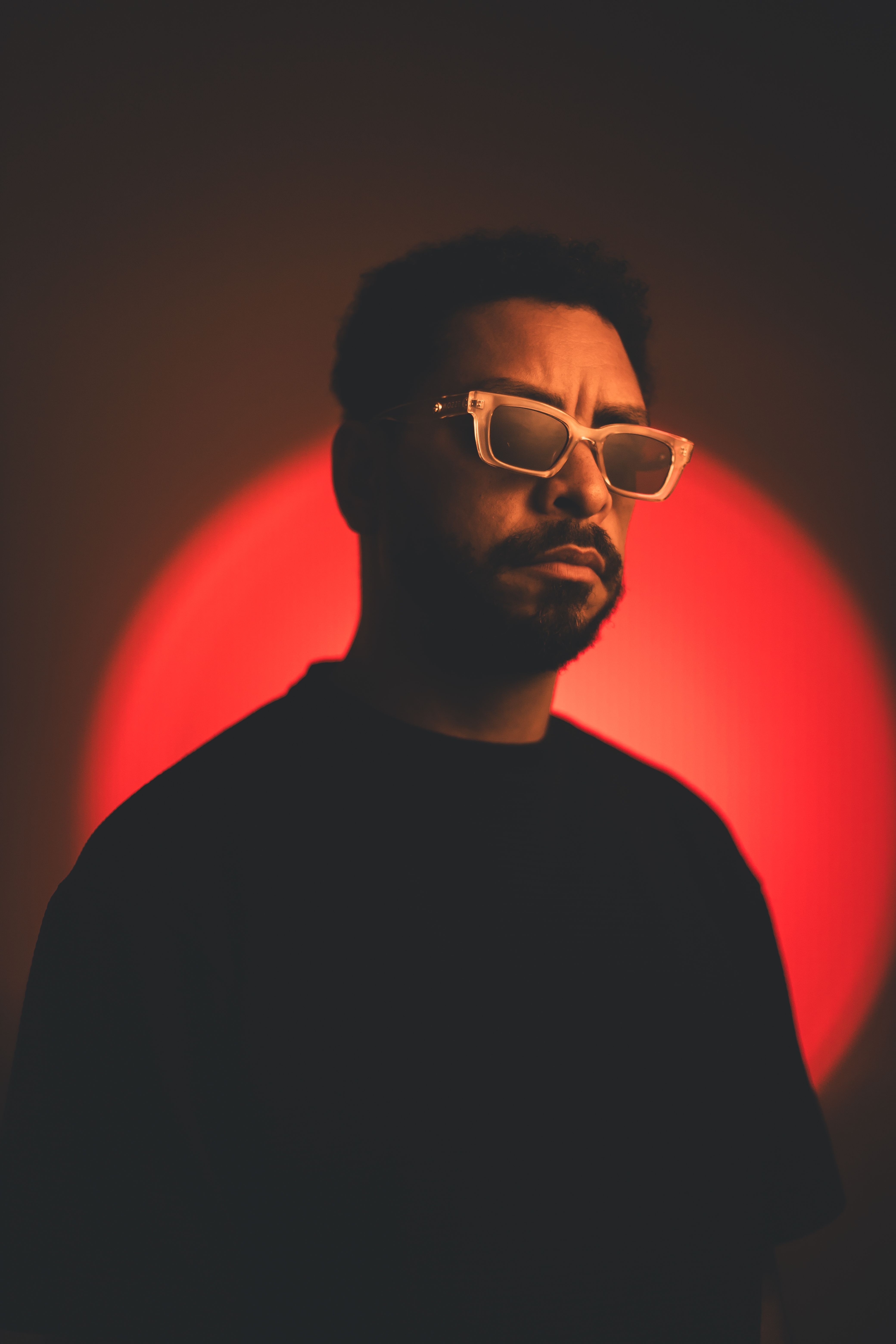 Artistic portrait of a man in glasses with a striking red halo effect, conveying a moody and conceptual vibe.