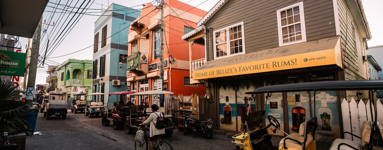 Bustling street in San Pedro, Belize featuring colorful buildings, golf carts, and a cyclist.