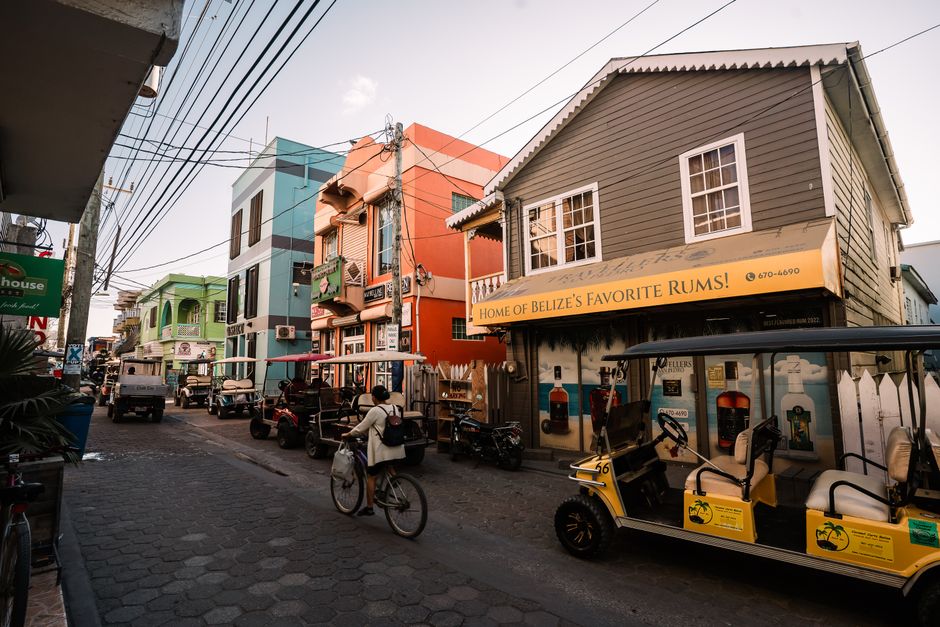 Bustling street in San Pedro, Belize featuring colorful buildings, golf carts, and a cyclist.