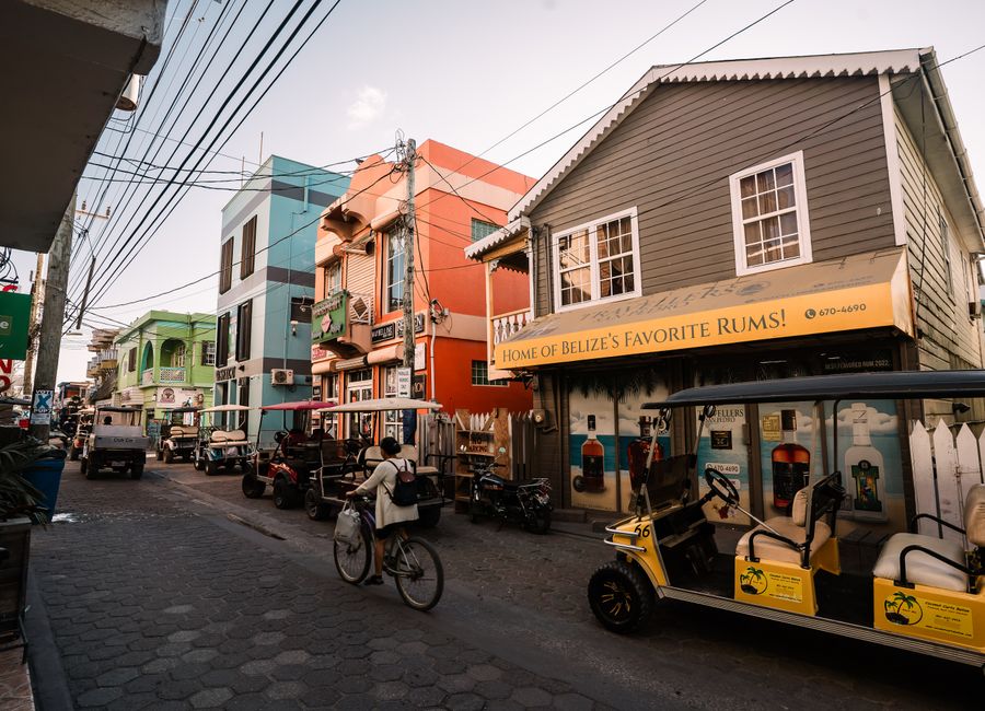Bustling street in San Pedro, Belize featuring colorful buildings, golf carts, and a cyclist.