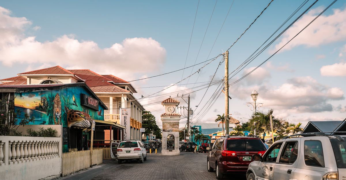 Sunny street scene with a clocktower and vibrant murals in Belizean town.