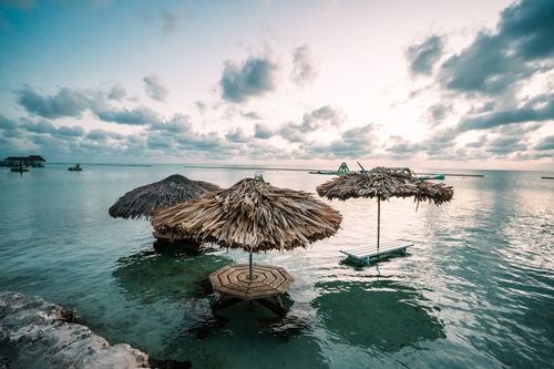 Free Peaceful beach setting with thatched umbrellas over calm ocean waters at sunset. Stock Photo