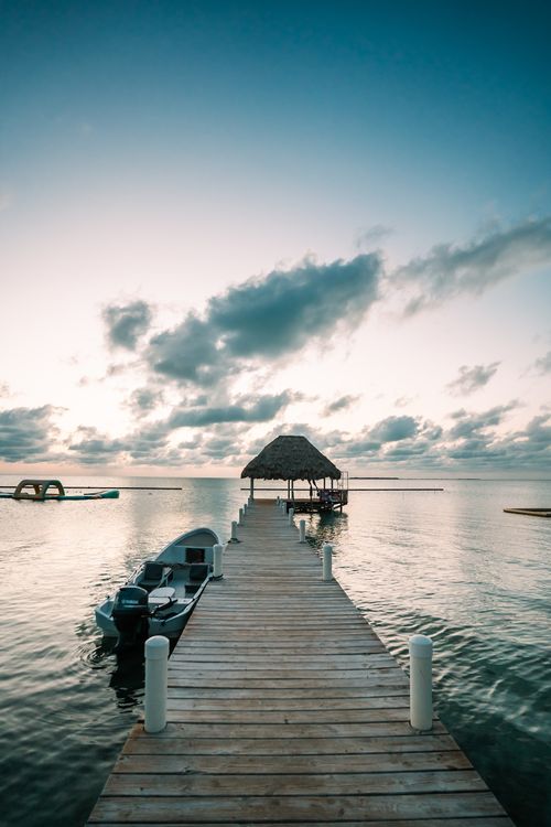 Free Idyllic view of a wooden pier extending into the calm sea under a tranquil sunrise sky. Stock Photo