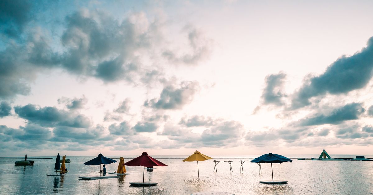 Peaceful beach setting with colorful parasols over calm waters in San Pedro, Belize at sunrise.