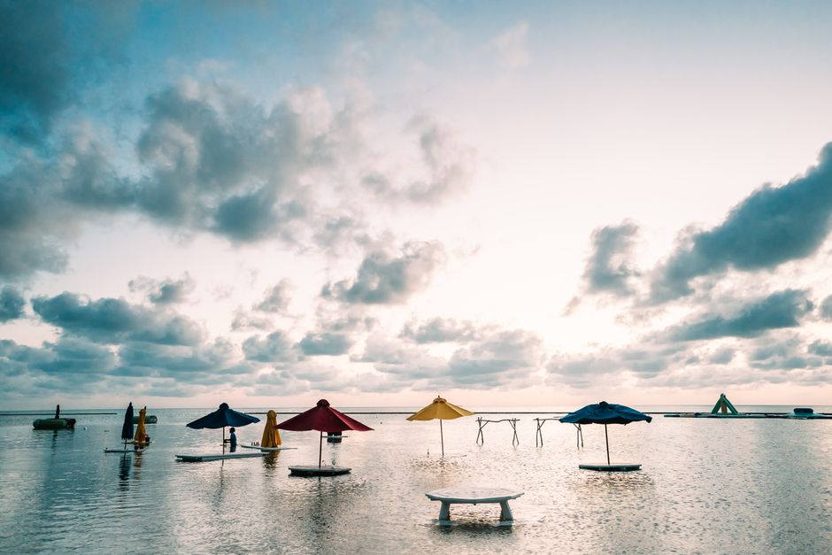 Peaceful beach setting with colorful parasols over calm waters in San Pedro, Belize at sunrise.