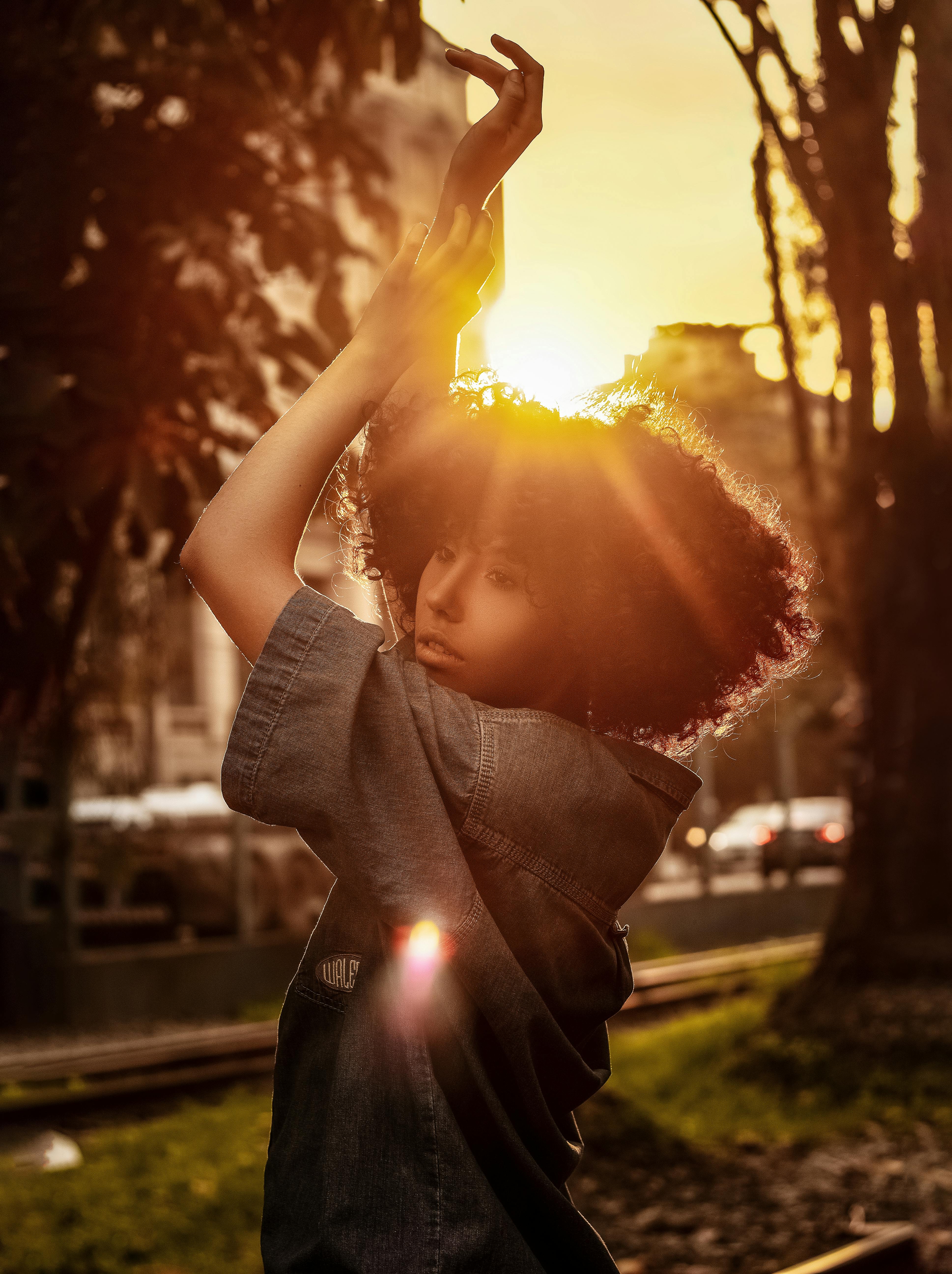 dreamy young ethnic lady dancing in city park during sundown