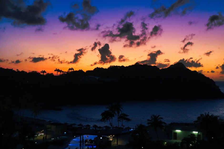 Capture of a vibrant purple and blue sunset over a tropical resort with silhouetted palm trees.