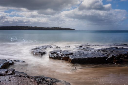 Long exposure of a serene Tasmanian seascape with rocky shore and cloudy sky.