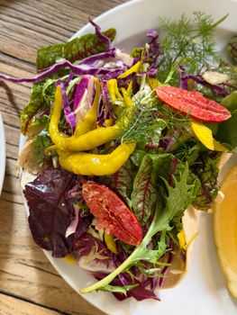 Vibrant salad with mixed greens, blood orange, and banana peppers on a wooden table.