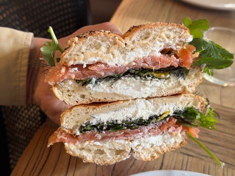 Close-up of a smoked salmon bagel sandwich with cream cheese and greens.