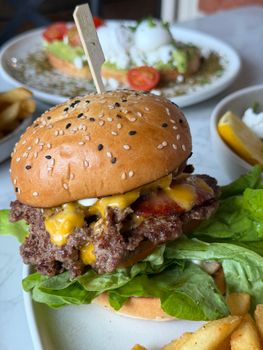 Delicious cheeseburger topped with bacon, lettuce, and cheddar. Perfect meal setting with fries.