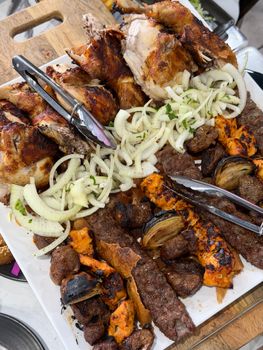 A vibrant platter of roasted chicken, assorted kebabs, and onions on a wooden board.