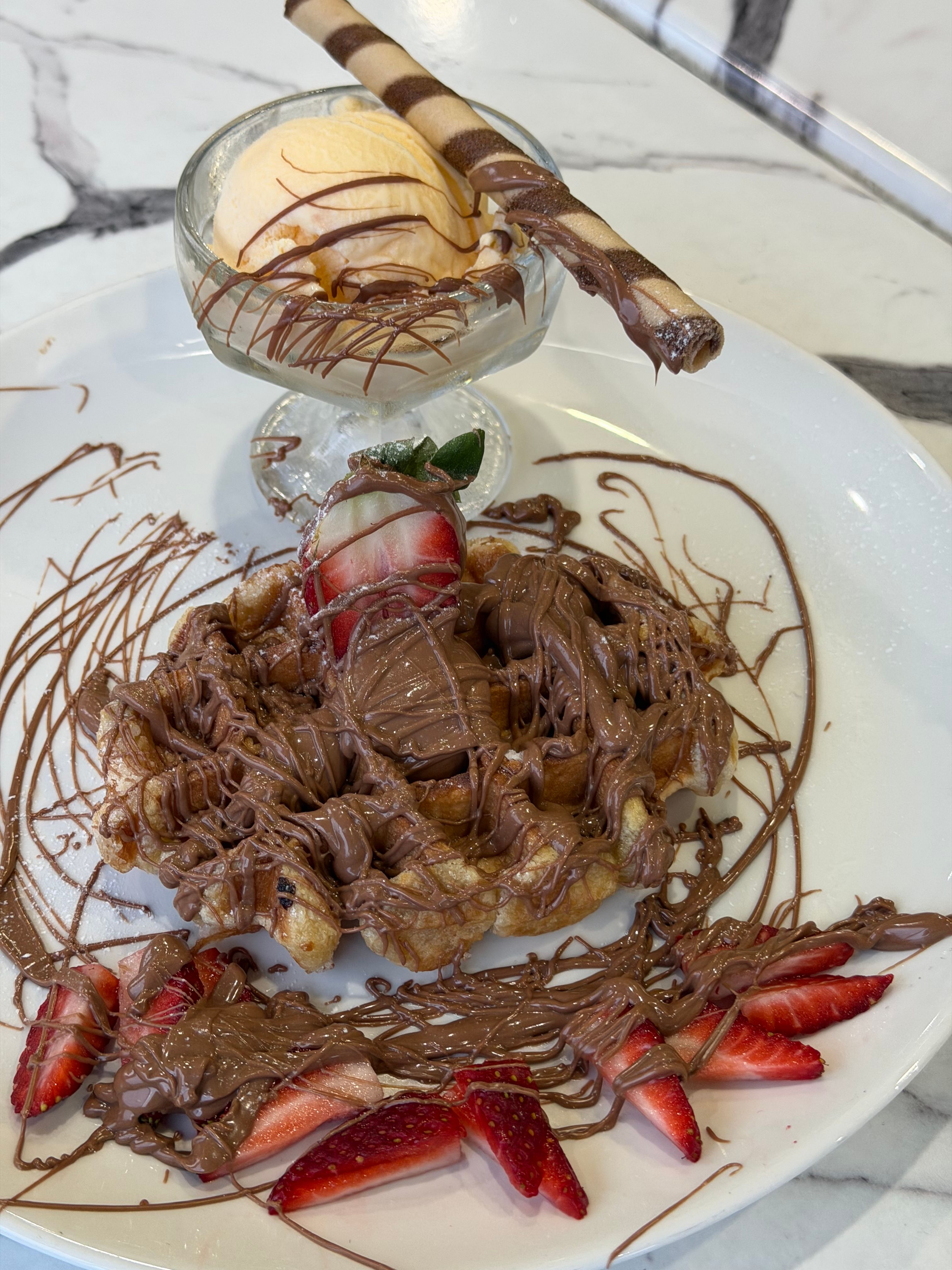 A scoop of creamy chocolate-hazelnut Nutella ice cream in a glass bowl, with visible swirls of Nutella and a dusting of chopped hazelnuts on top.