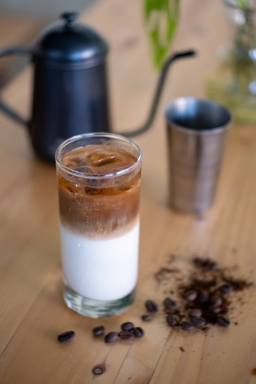 Free A refreshing glass of iced coffee with milk on a wooden table, coffee beans scattered around. Stock Photo