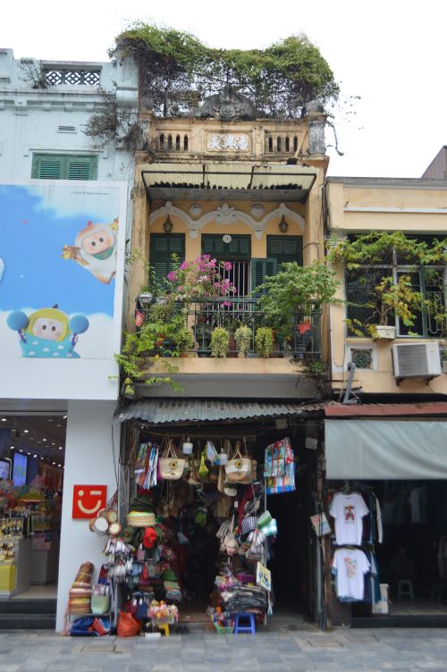 Free A picturesque shopfront in Hanoi featuring a floral-adorned balcony above a bustling street market. Stock Photo