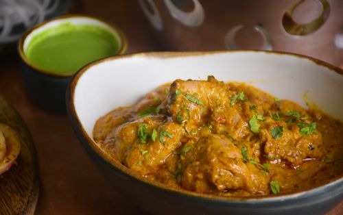 Free Delicious Indian chicken curry served in a bowl, garnished with fresh cilantro, alongside green chutney. Stock Photo