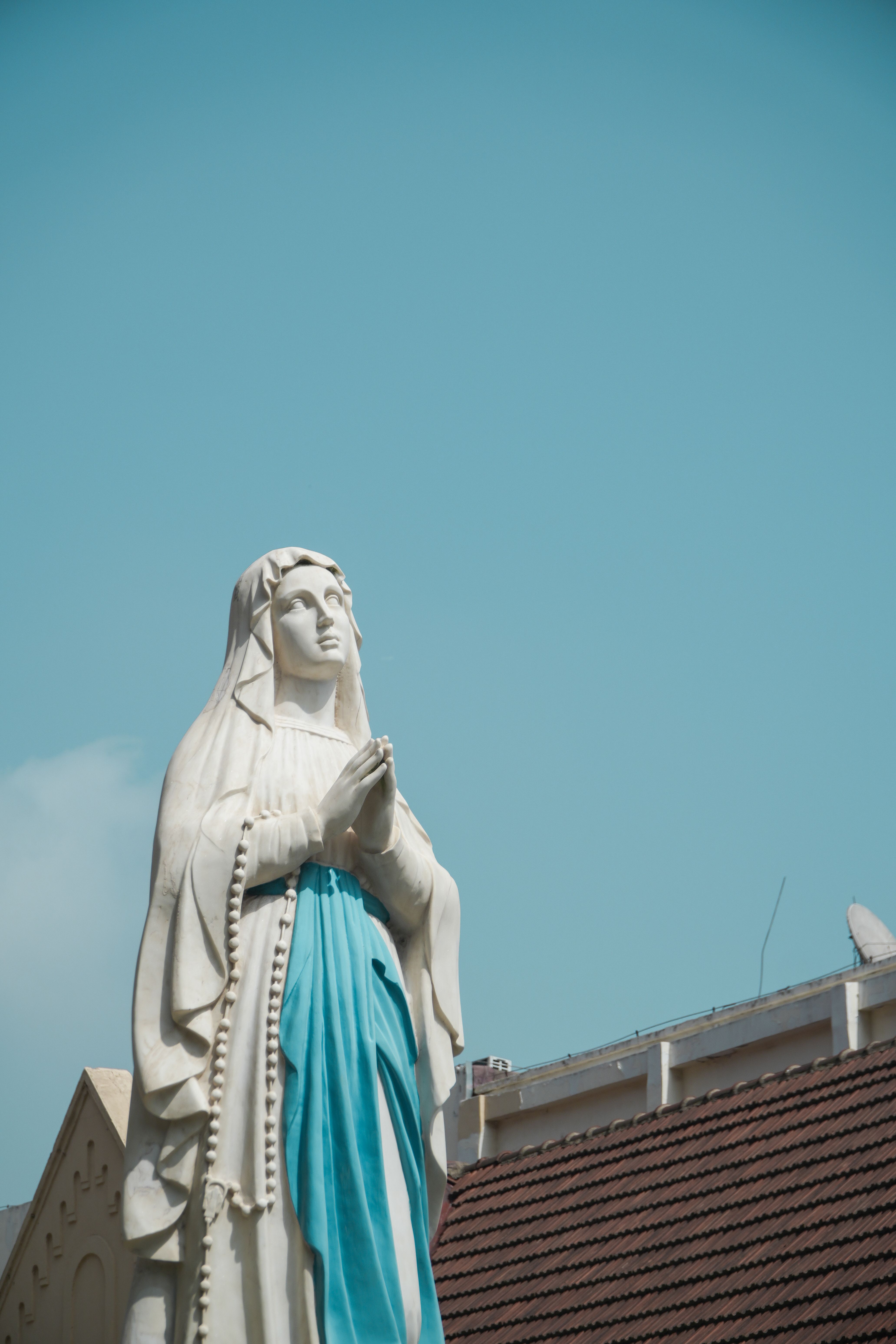 Serene statue of the Virgin Mary in prayer set against a clear blue sky, evoking peace and spirituality.