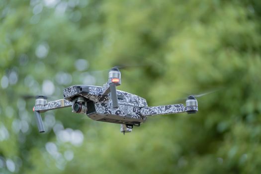 A stylish drone with graffiti design flying outdoors in a lush green environment.