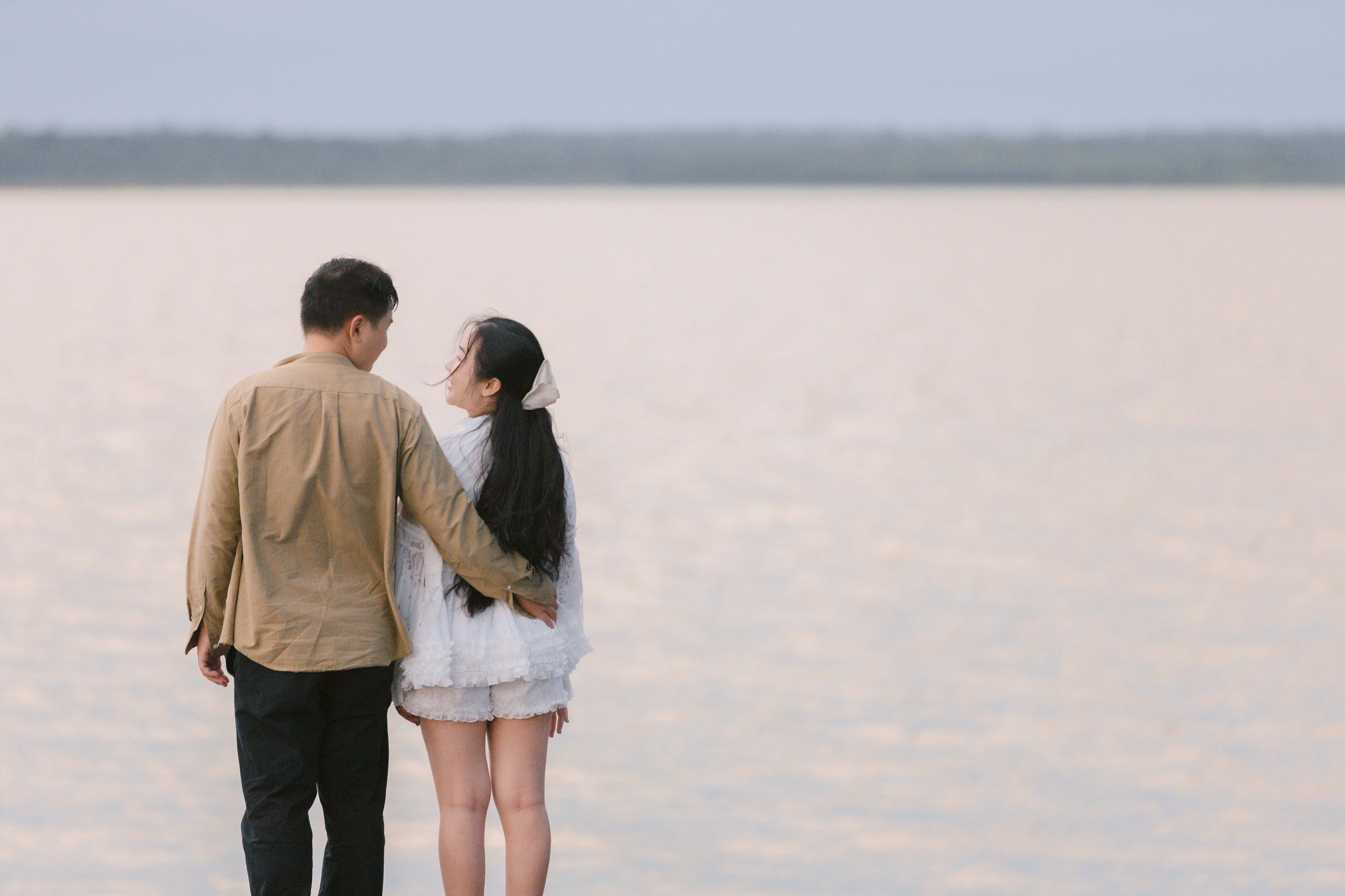 A couple embraces by a serene lakeside at sunset, sharing a loving moment.