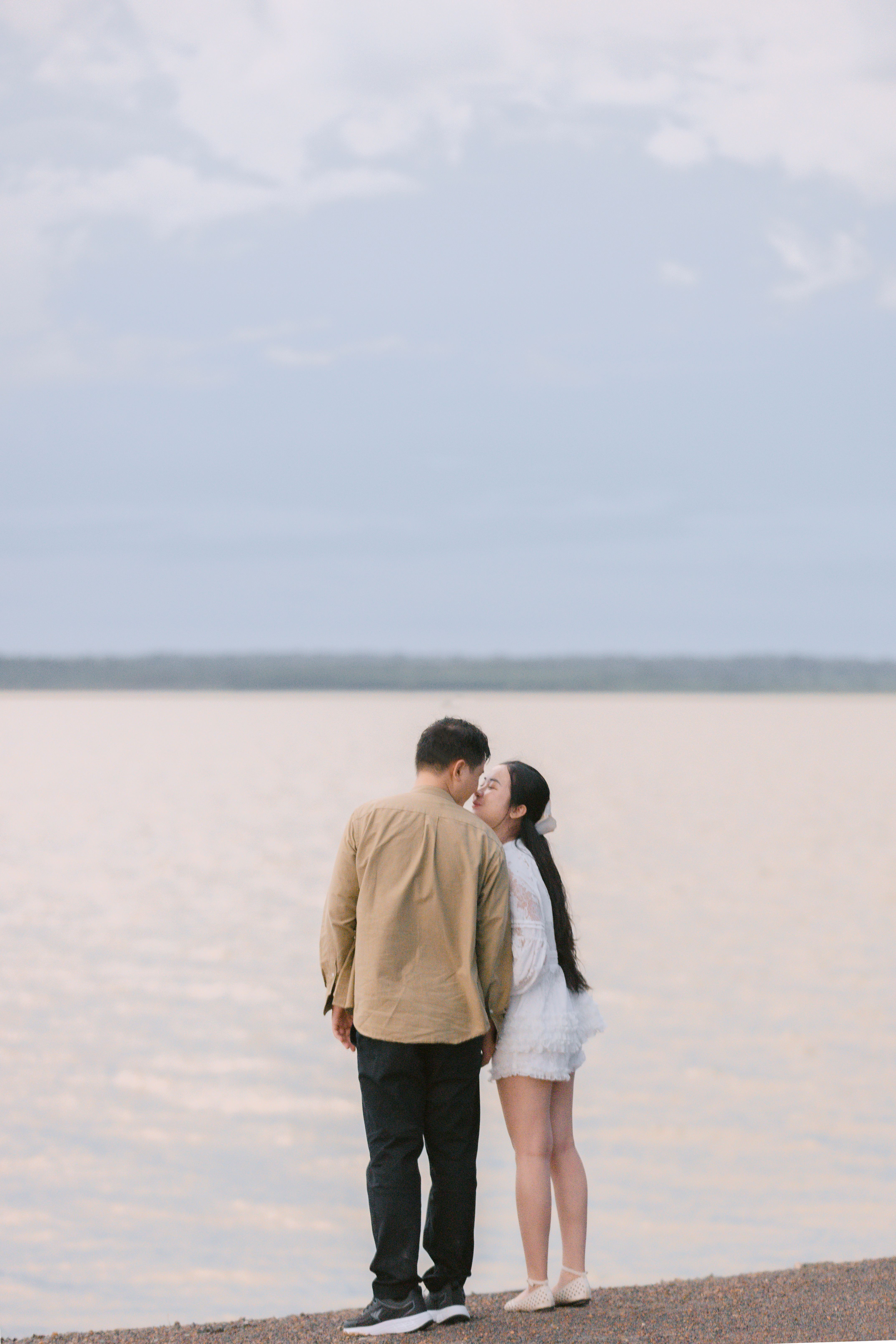 A couple shares a kiss by a serene lakeside, under a calm sky, symbolizing romance and tranquility.