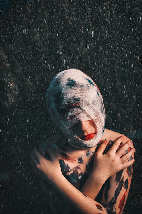 Free From above of melancholic injured anonymous female with head and face covered with bandage and paints on body Stock Photo