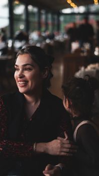A candid moment of a smiling woman with a child in a warmly lit restaurant, capturing joy and connection.