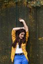 Confident young woman with arms over head near weathered fwall