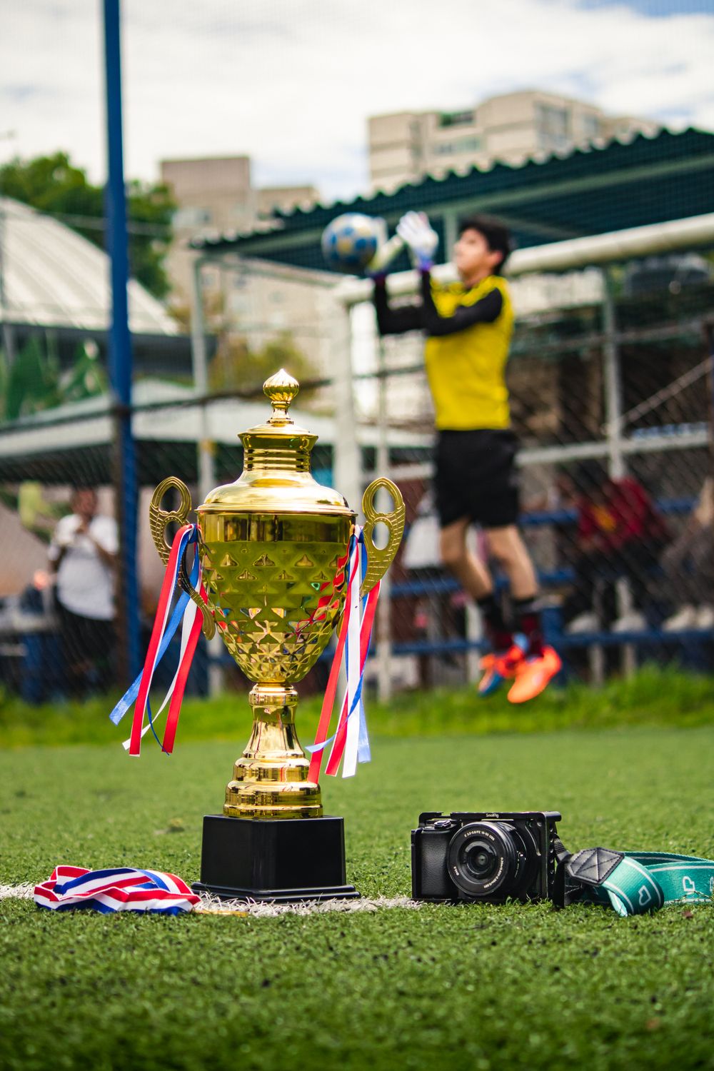 Golden championship trophy on the pitch with a goalkeeper in action in the background
