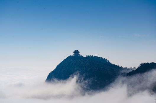 Serene view of a pagoda atop misty Mount Emei, surrounded by clouds and blue sky.