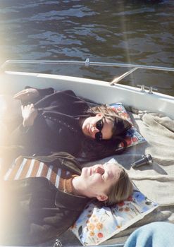 Two women enjoy a sunny day relaxing on a boat in Amsterdam canals.